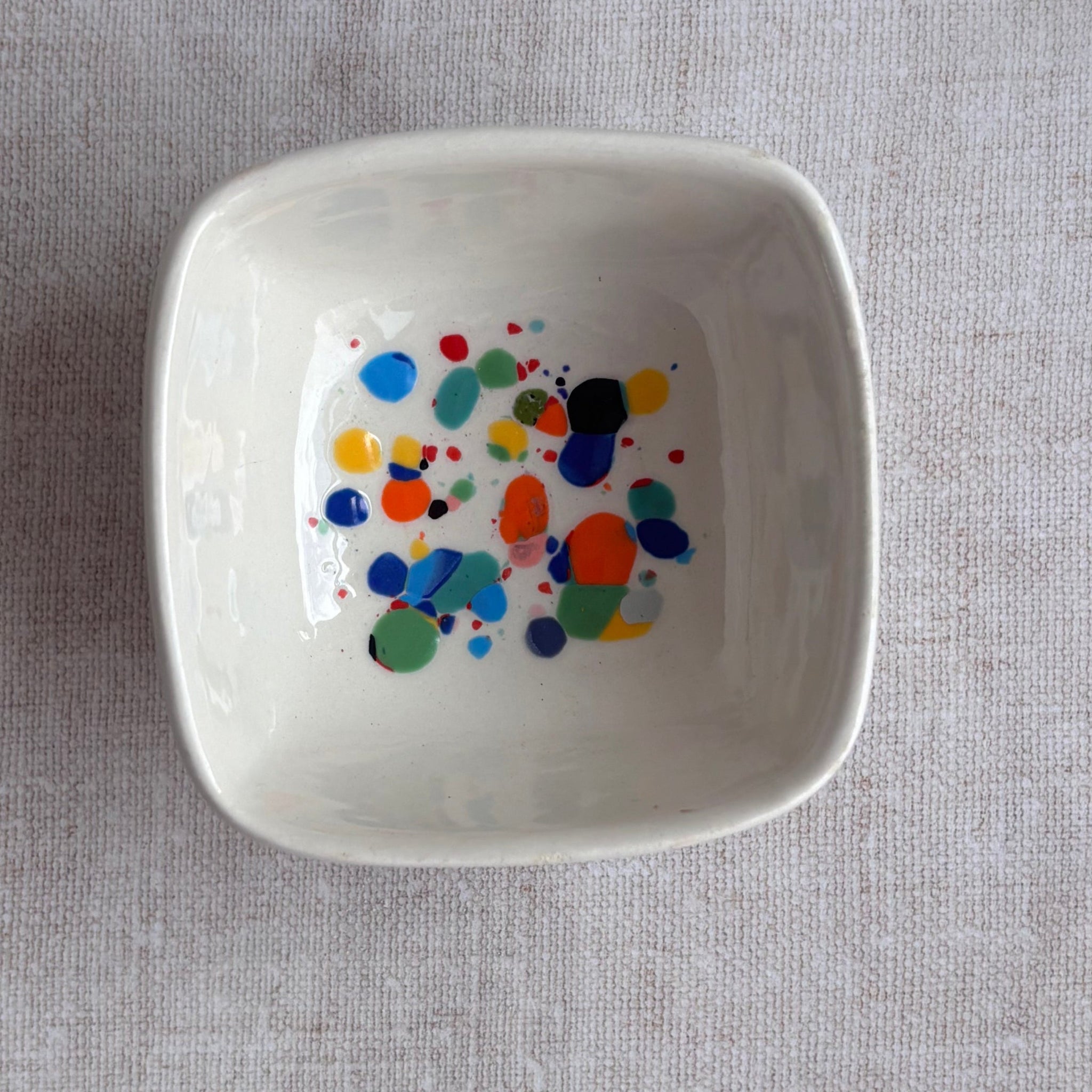 White ceramic bowl with colorful dot pattern on a gray fabric background