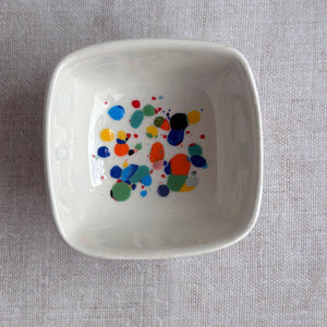 White ceramic bowl with colorful dot pattern on a gray fabric background
