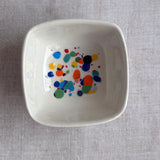 White ceramic bowl with colorful dot pattern on a gray fabric background